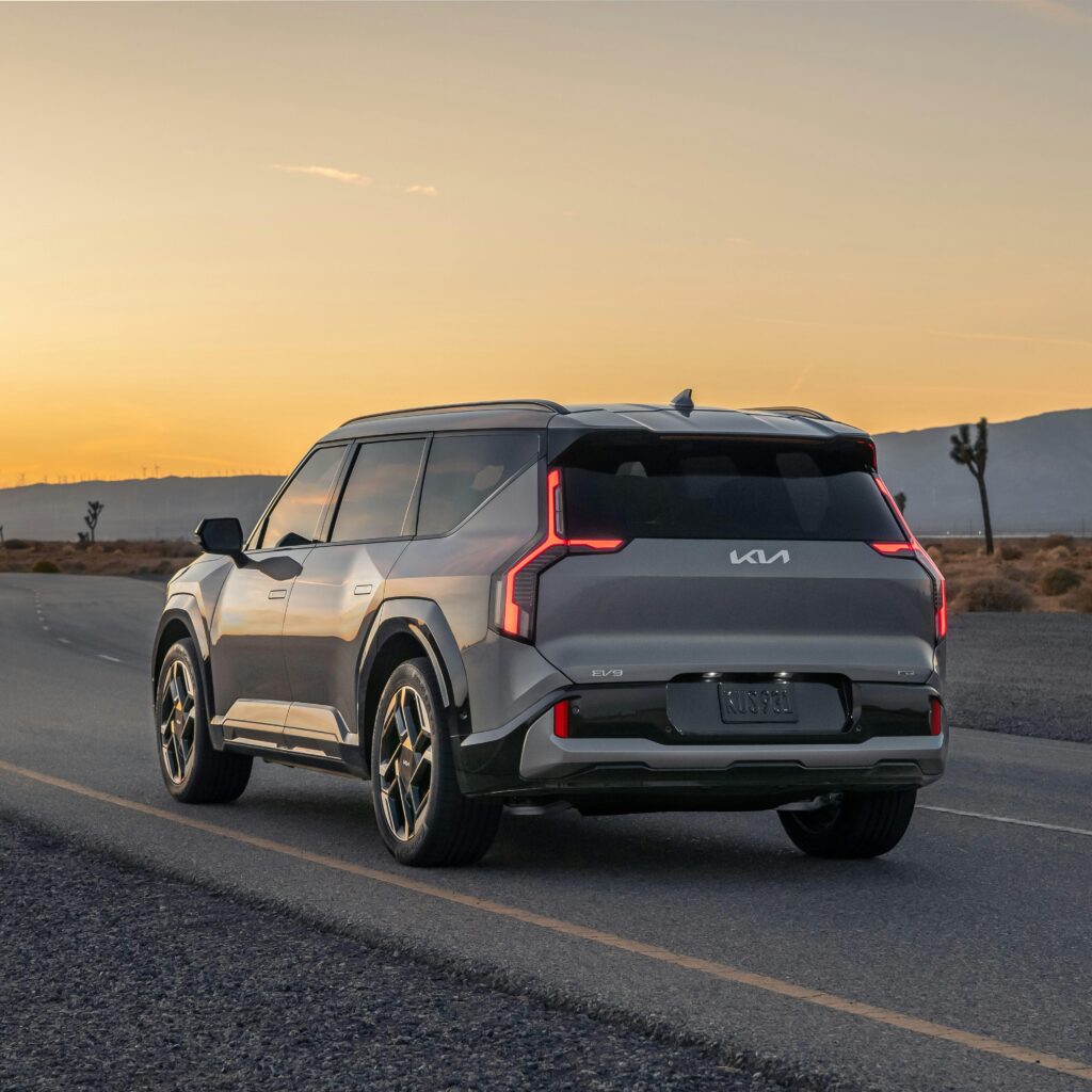 Kia EV9 GT driving on an open road at sunset, showcasing modern electric vehicle design.